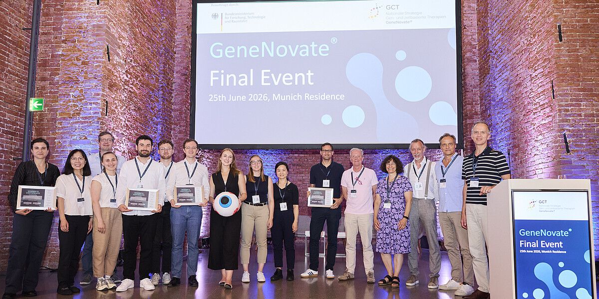 Zu sehen sind 16 lächelnde Menschen auf einer Bühne. Die vier Gewinner:innen halten gerahmte Auszeichnungen in den Händen.