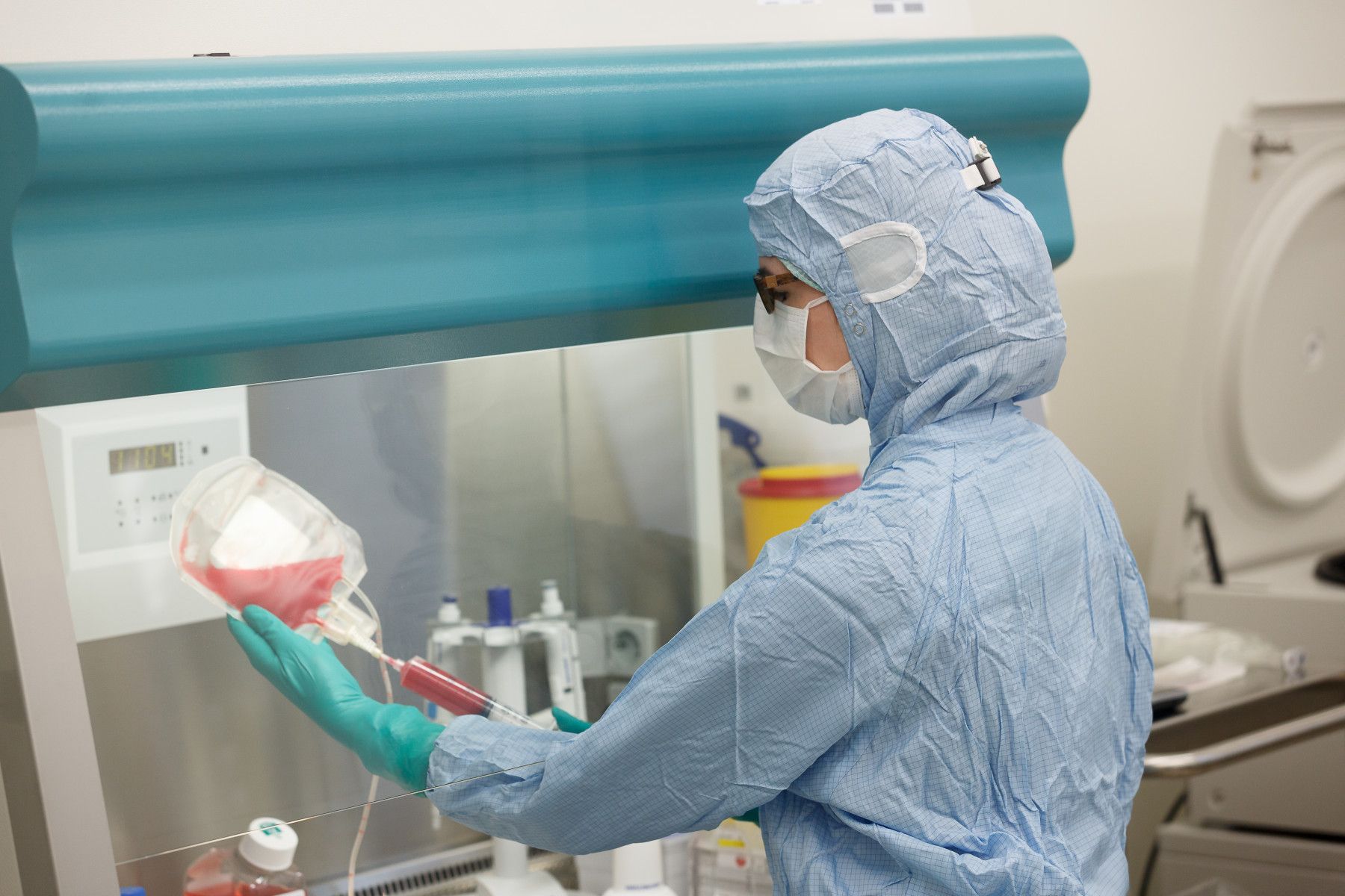 Person in Schutzkleidung und Maske bei der Arbeit mit einer Blutprobe in einem medizinischen Labor.
